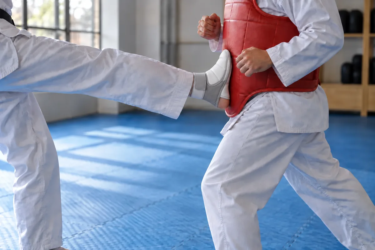 A front foot in a white foot protector pressed against the red trunk protector of a fighter stepping in.